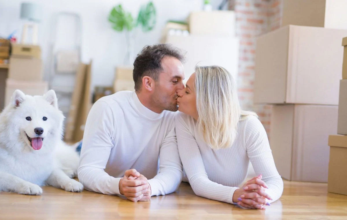 Young beautiful couple with dog lying down on the floor at new home around cardboard boxes