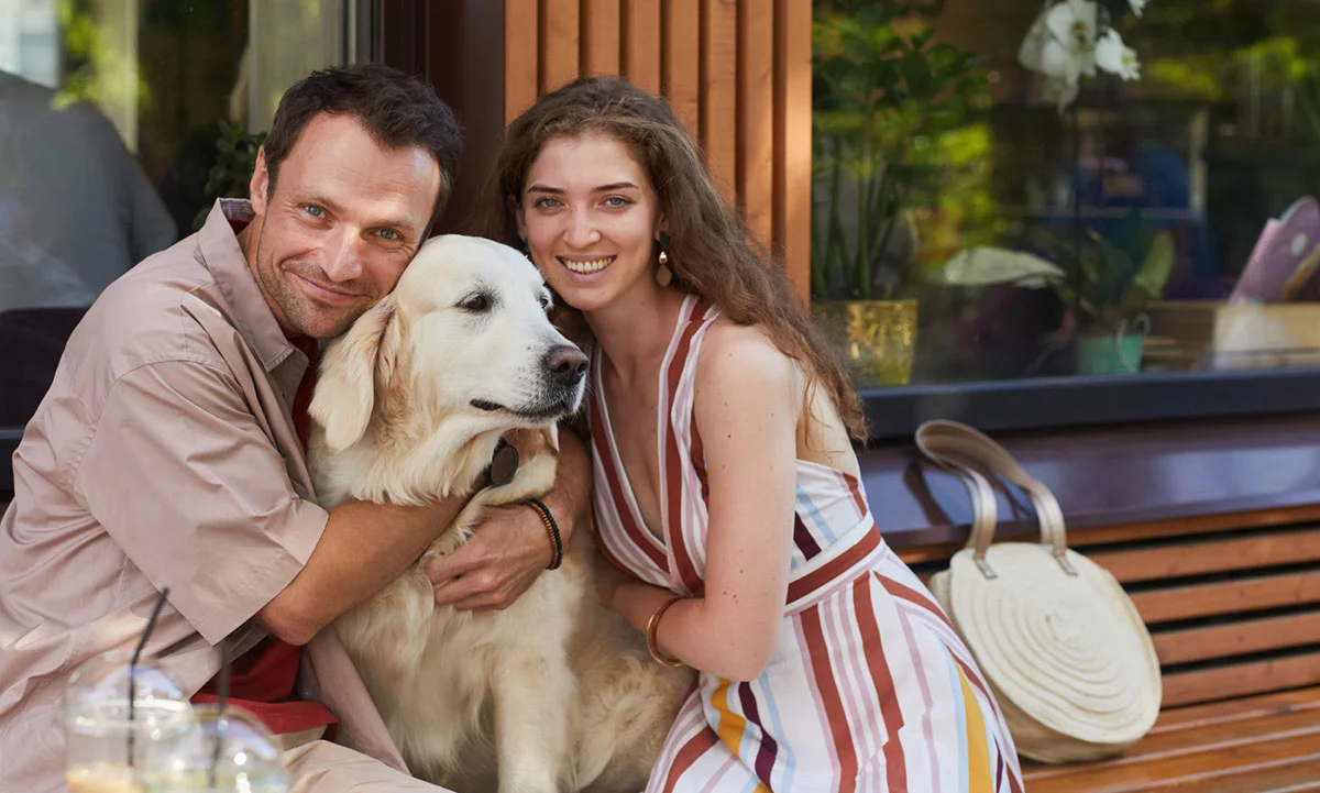 Portrait of happy couple embracing dog outdoors and looking at camera in Summer, copy space